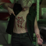 Model wearing pentagram carved into chest flesh silicone prosthetic attached to round neck mesh sleeveless shirt